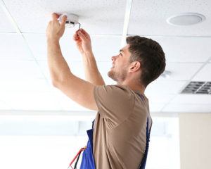 smoke detector being installed by young man onto the ceiling