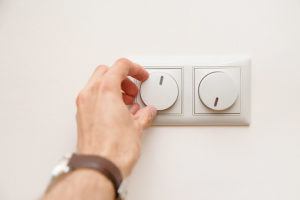 Human hand turning down electrical light dimmer switch to dim the lights and conserve energy