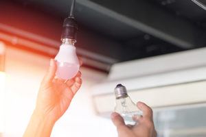 Person changing out a traditional incandescent light bulbs with new energy saving LED light bulbs.