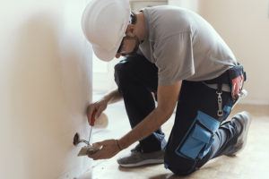 Professional electrician removing old electrical wiring from behind a wall socket