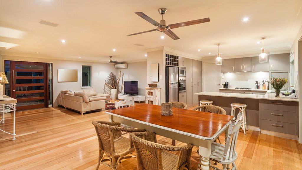 Open kitchen and family area with ceiling fans, one near wall-mounted heating unit. 