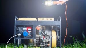 generator on grass with work light held over it by off-camera hand
