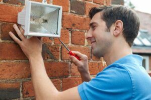 Man with screwdriver installing a security light on a brick exterior wall
