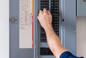 man's arm, with hand on circuit breaker in electrical panel.