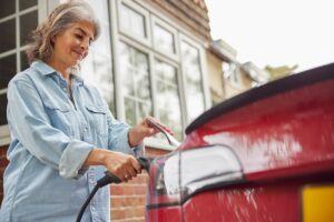 Senior woman plugging in a car charger into her EV in front of her house.