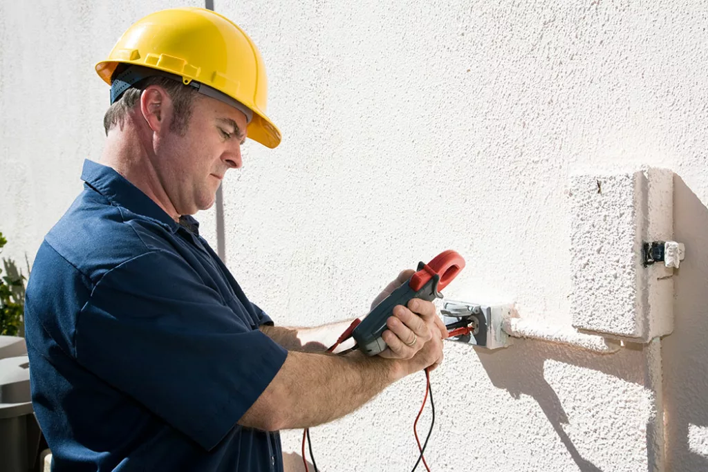 electrician with volt meter, checking outdoor outlet on stuccoed wall