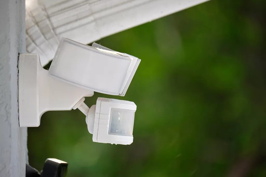 White motion-sensor security light mounted on stucco outer wall of home. 