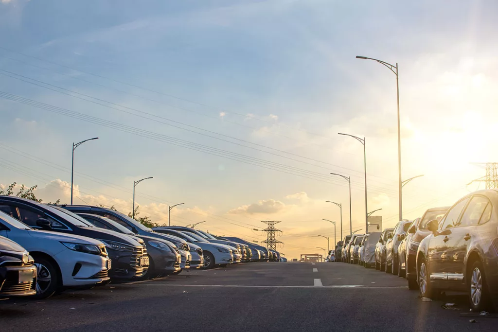 A parking lot at sunset, featuring rows of cars and commercial parking lot lighting.