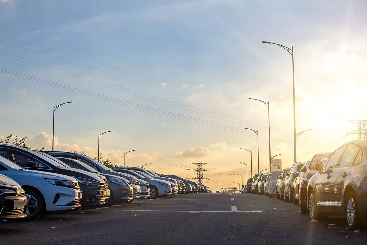A parking lot at sunset, featuring rows of cars and commercial parking lot lighting.