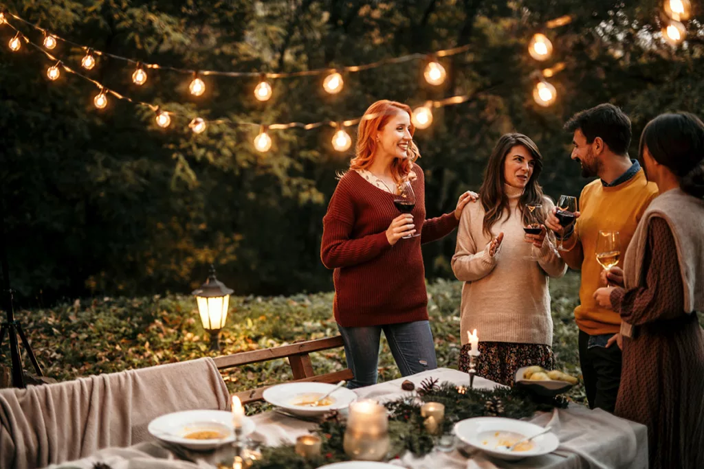 A group of people celebrate in an outdoor eating area with LED string lights.