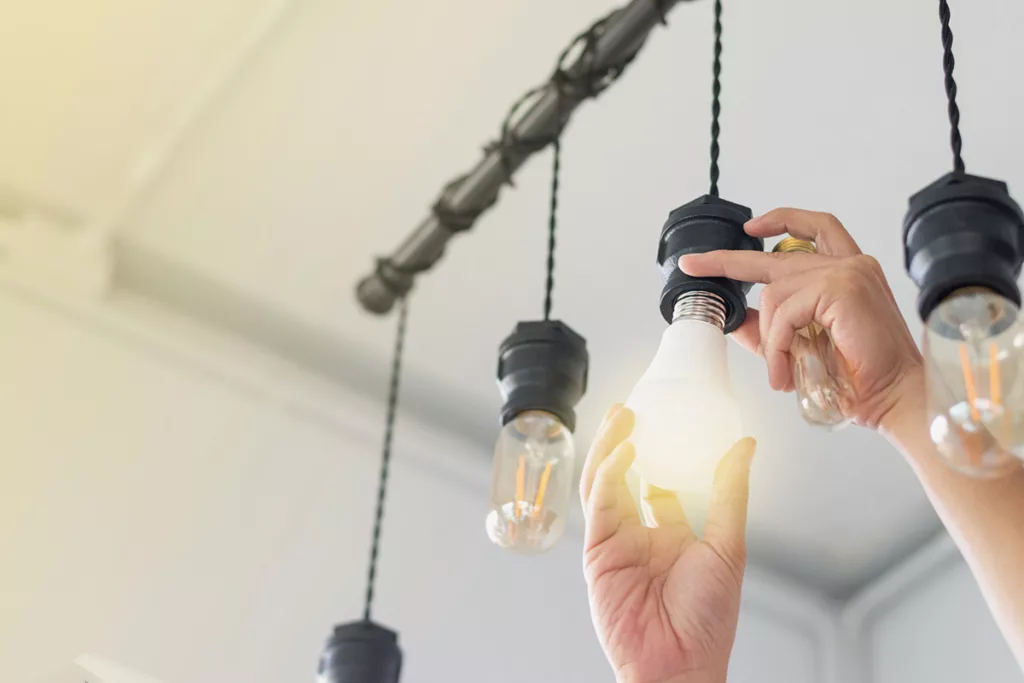 Two hands change out an incandescent light bulb to replace it with an LED light bulb.
