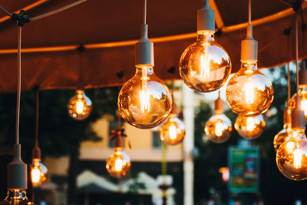 Incandescent lightbulbs hang from the ceiling in an outdoor cafe.