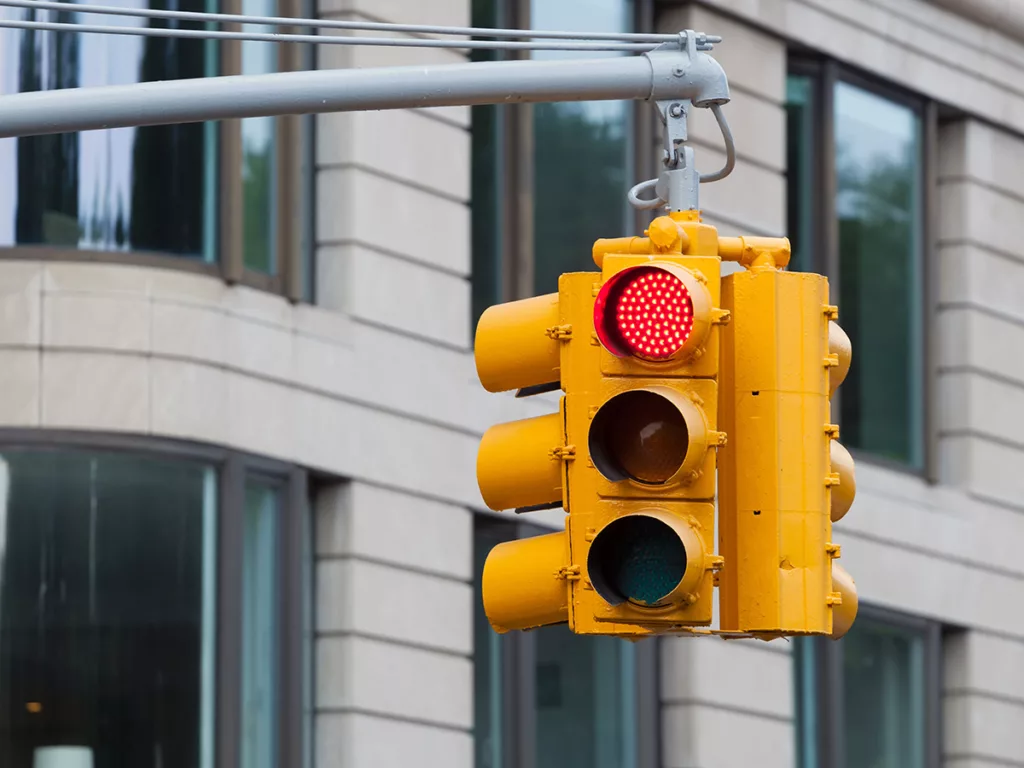 A yellow traffic light hangs from a pole in front of a brick building