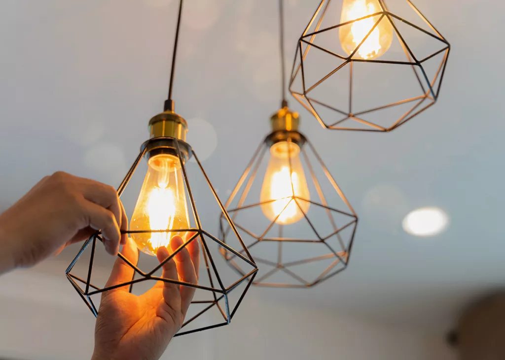 A hand changes out the lightbulb in a light fixture hanging from a white ceiling.