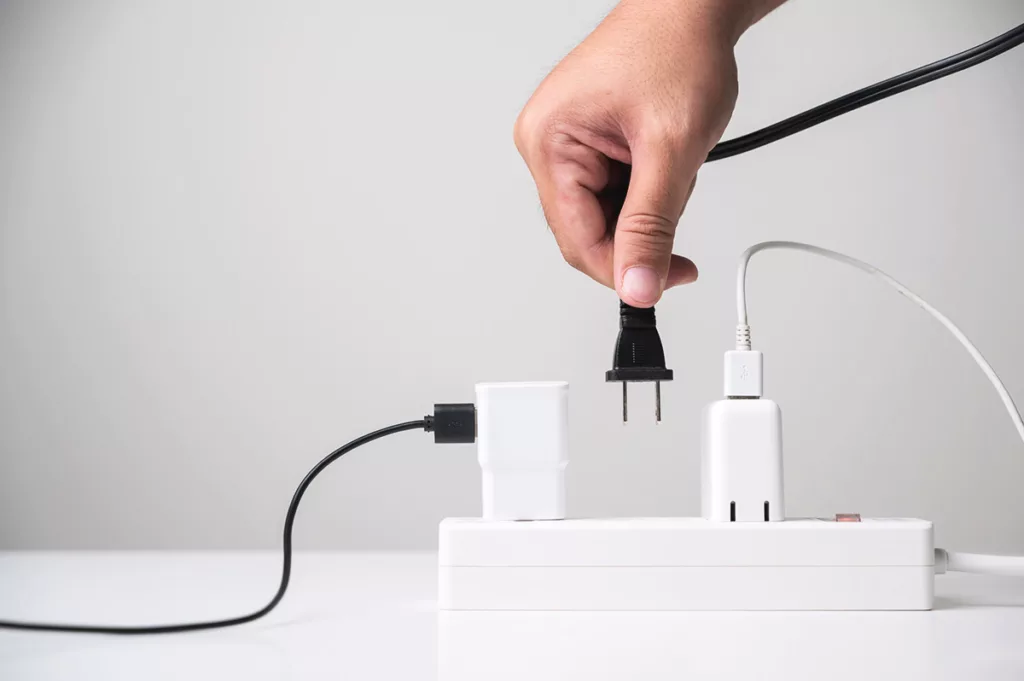 A hand holds an electronic cord, unplugging an unused lamp to save energy during the holiday season.