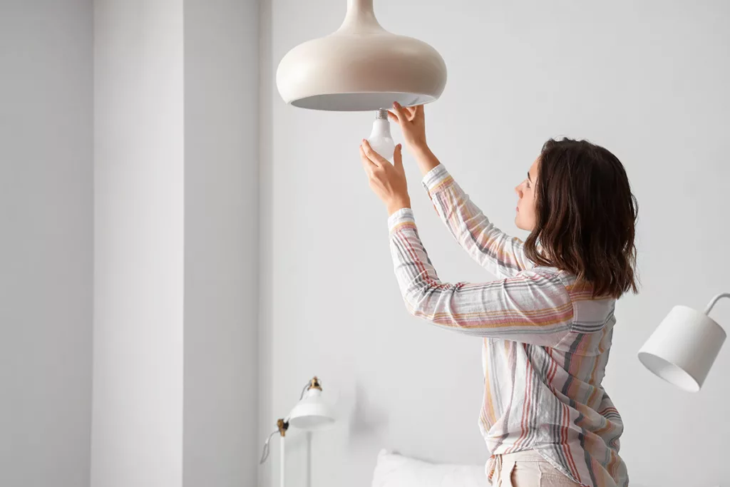 A woman in a white room dusts a light bulb to save energy.
