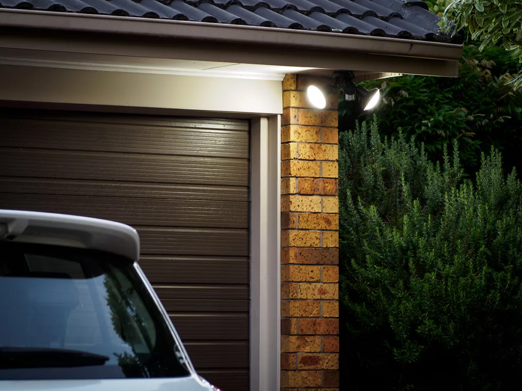 The exterior of a home with a black garage door and security flood lights with bright LED light bulbs