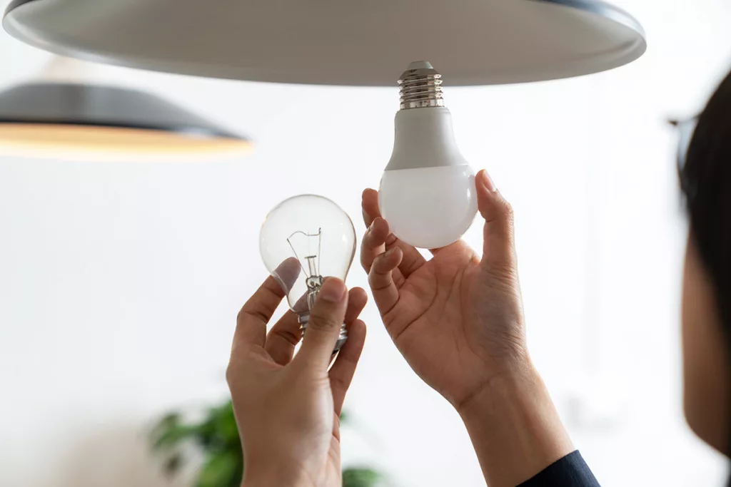 Two hands changing the lightbulb of a lighting fixture to an energy efficient LED lightbulb