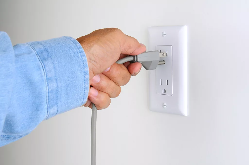 Close up of a hand unplugging an unused electronic cord to save energy and lower the electricity bill.