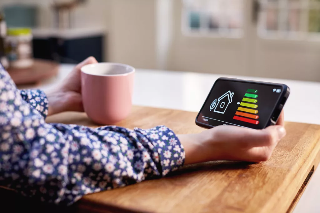 A close up of a woman holding her phone and a cup of coffee, monitoring her energy usage on an app.