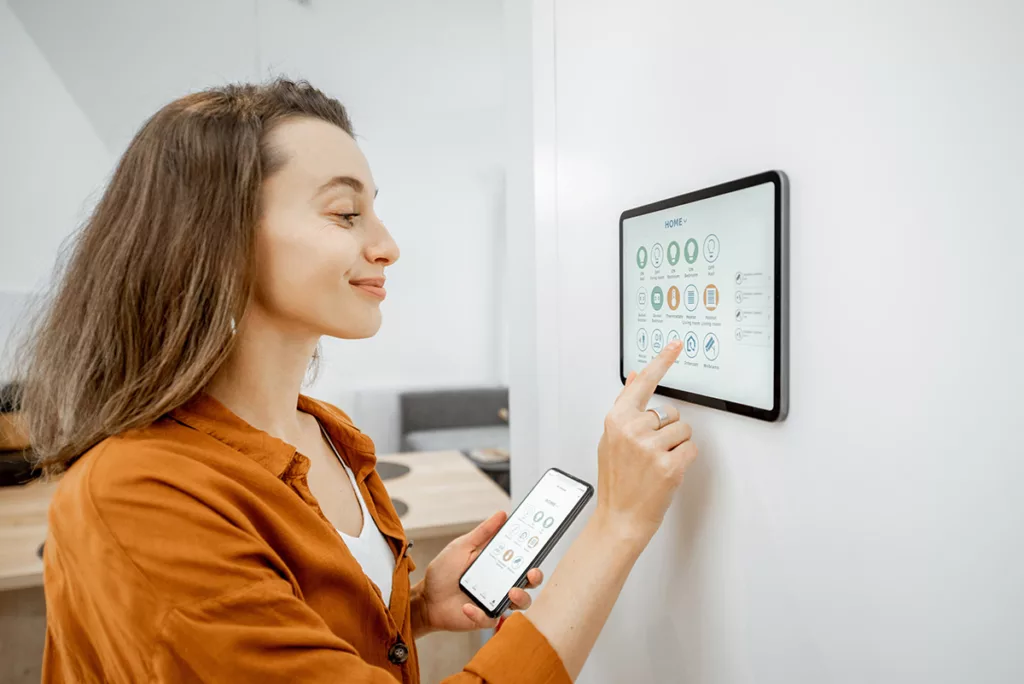 A young woman controls her home security system with a tablet on the wall.