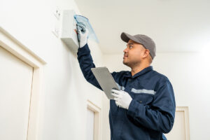 An electrician in a uniform, holding a clipboard and completing an electrical inspection for home safety