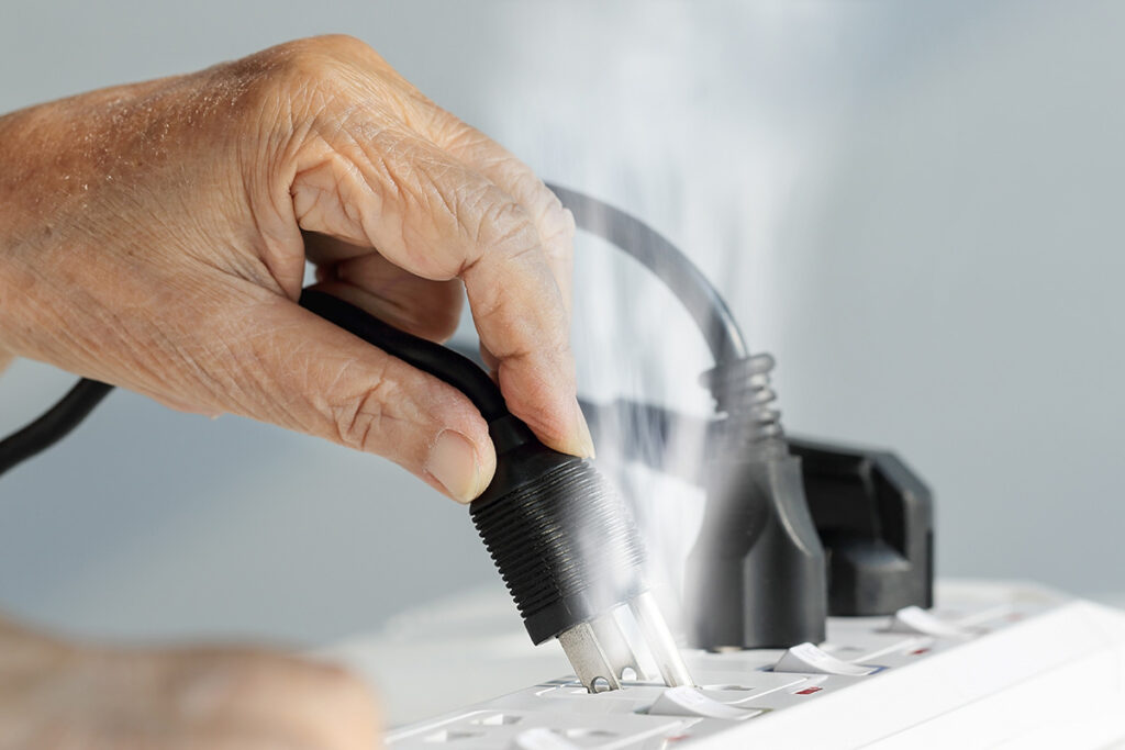A hand plugging a cord into an electrical outlet producing smoke