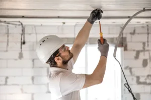 An electrician in a white shirt and hard hat repairs commercial lighting for a business