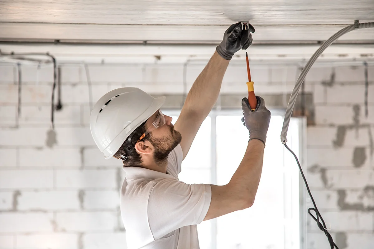 An electrician in a white shirt and hard hat repairs commercial lighting for a business